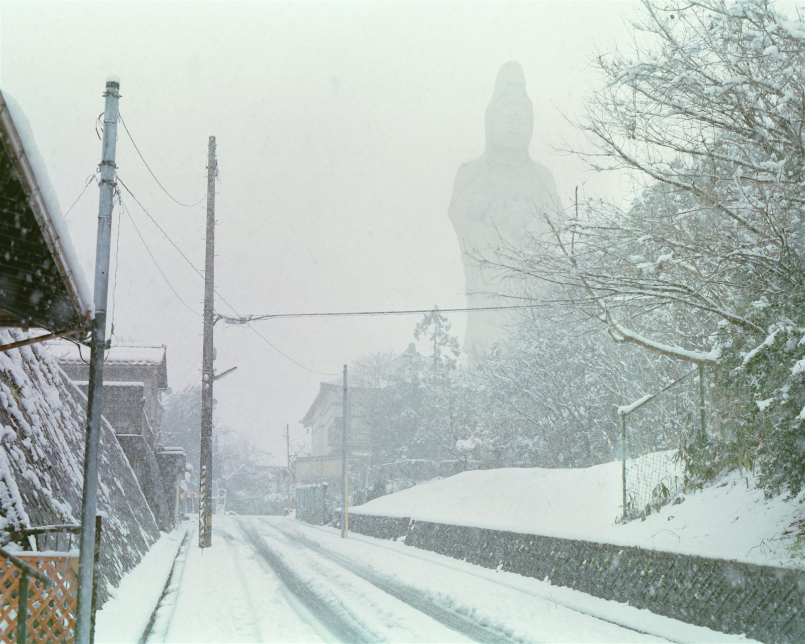 雪の降る坂道と遠くにかすむ観音像